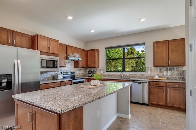 kitchen featuring stainless steel appliances, decorative backsplash, light stone counters, and a center island