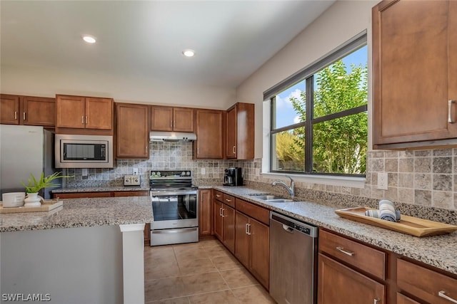 kitchen with appliances with stainless steel finishes, tasteful backsplash, sink, and light stone counters