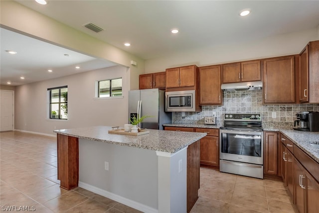 kitchen featuring light stone counters, stainless steel appliances, a kitchen island, light tile patterned floors, and decorative backsplash