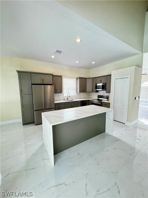 kitchen with a center island, stainless steel appliances, light stone counters, and sink