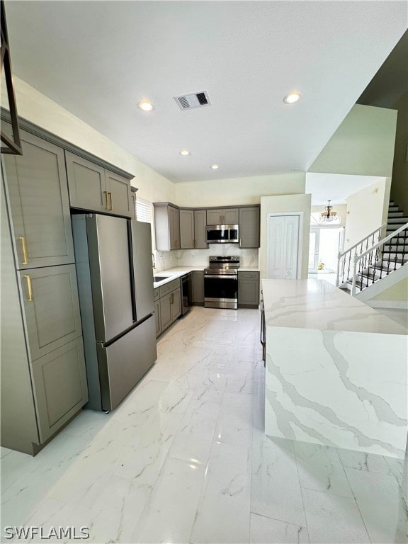 kitchen with gray cabinets, light stone countertops, and appliances with stainless steel finishes