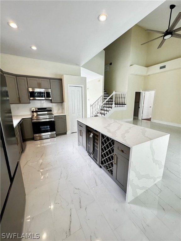 kitchen with light stone countertops, a towering ceiling, stainless steel appliances, and ceiling fan