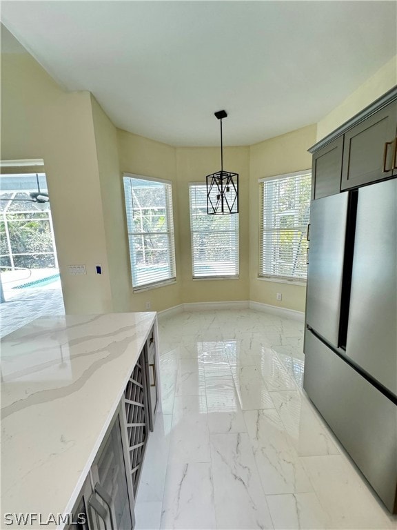 kitchen featuring light stone countertops, stainless steel fridge, and hanging light fixtures