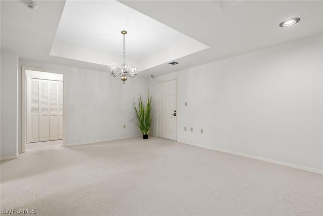 carpeted empty room with a notable chandelier and a tray ceiling