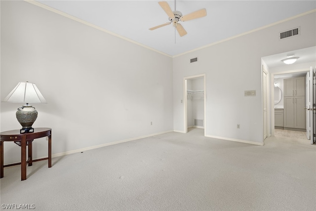 unfurnished bedroom featuring light carpet, ornamental molding, ceiling fan, a spacious closet, and a closet