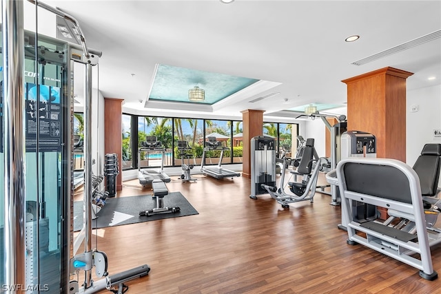 exercise room featuring a tray ceiling, floor to ceiling windows, ceiling fan, and hardwood / wood-style flooring