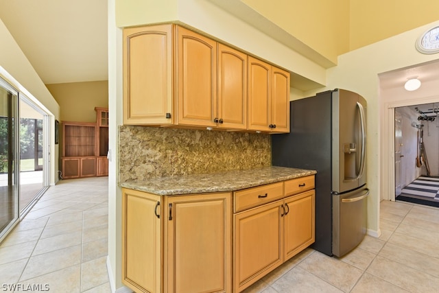 kitchen with light tile floors, tasteful backsplash, stainless steel fridge, vaulted ceiling, and light stone countertops