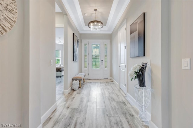 foyer featuring crown molding, light hardwood / wood-style flooring, a notable chandelier, and a tray ceiling