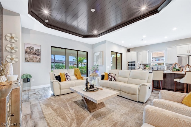 living room featuring ornamental molding, light hardwood / wood-style flooring, a wealth of natural light, and a tray ceiling