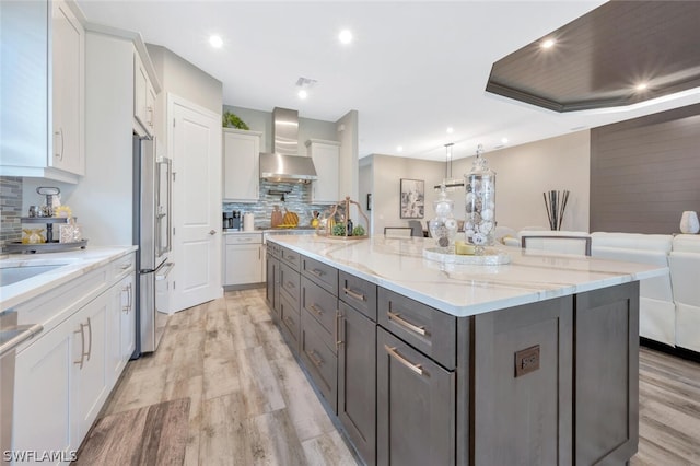 kitchen featuring backsplash, light hardwood / wood-style flooring, a large island, wall chimney exhaust hood, and white cabinets