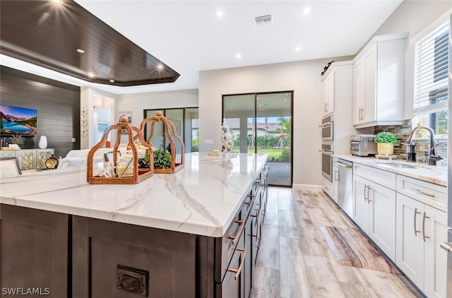 kitchen with light stone counters, white cabinets, sink, a tray ceiling, and light hardwood / wood-style flooring