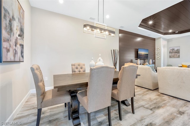 dining area with an inviting chandelier, a tray ceiling, and light wood-type flooring