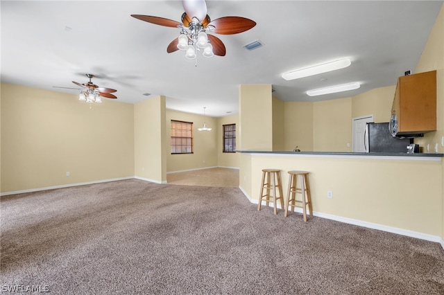 kitchen featuring carpet flooring, kitchen peninsula, ceiling fan, refrigerator, and a breakfast bar