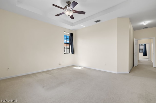 spare room with ceiling fan, a raised ceiling, and carpet