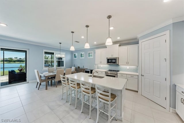 kitchen with white cabinets, hanging light fixtures, appliances with stainless steel finishes, a kitchen breakfast bar, and a kitchen island with sink