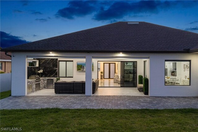 back house at dusk featuring a yard, a patio, and an outdoor kitchen