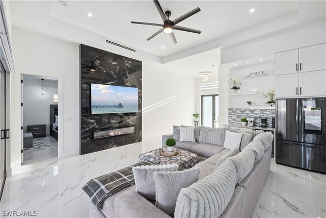 living room featuring a raised ceiling, ceiling fan, and a high end fireplace