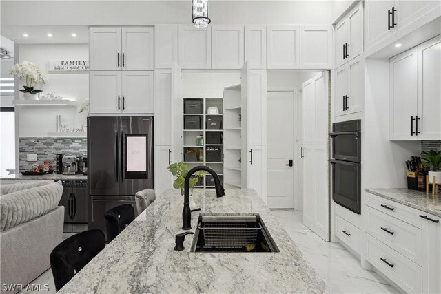 kitchen with sink, light stone counters, refrigerator, black double oven, and white cabinets