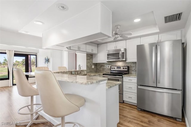 kitchen featuring white cabinetry, stainless steel appliances, kitchen peninsula, light hardwood / wood-style floors, and a breakfast bar