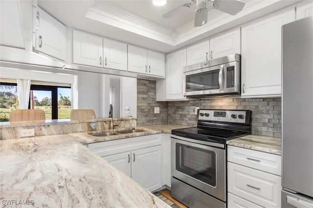 kitchen with light stone countertops, white cabinetry, sink, stainless steel appliances, and ornamental molding