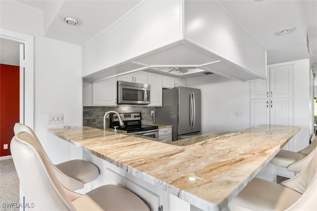 kitchen with backsplash, white cabinets, a breakfast bar area, kitchen peninsula, and stainless steel appliances