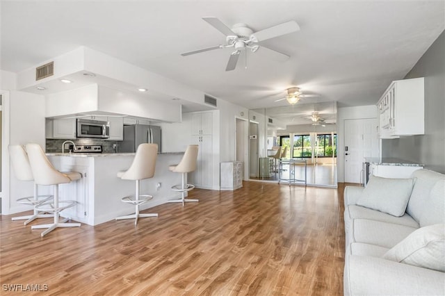 kitchen featuring kitchen peninsula, appliances with stainless steel finishes, a breakfast bar, white cabinets, and light hardwood / wood-style floors