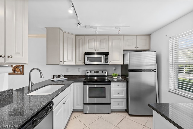 kitchen with rail lighting, stainless steel appliances, light tile floors, sink, and dark stone counters