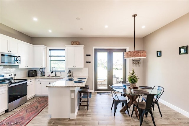 kitchen featuring white cabinetry, sink, hanging light fixtures, stainless steel appliances, and a kitchen island