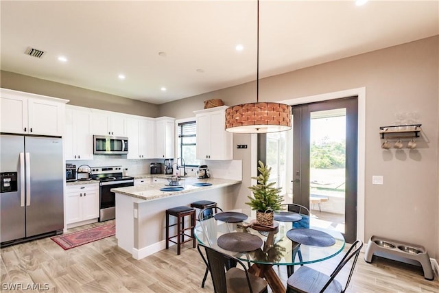 kitchen featuring kitchen peninsula, appliances with stainless steel finishes, a wealth of natural light, white cabinets, and hanging light fixtures