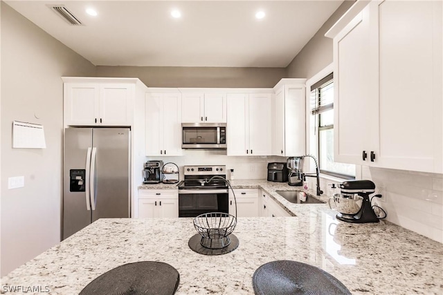 kitchen featuring light stone countertops, appliances with stainless steel finishes, tasteful backsplash, sink, and white cabinets