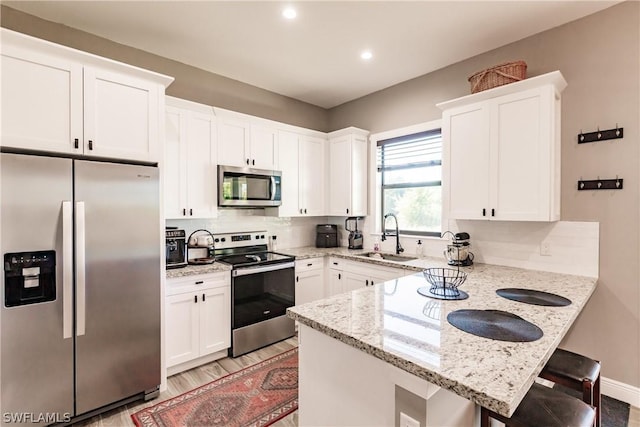 kitchen with appliances with stainless steel finishes, a kitchen breakfast bar, light stone counters, sink, and white cabinets