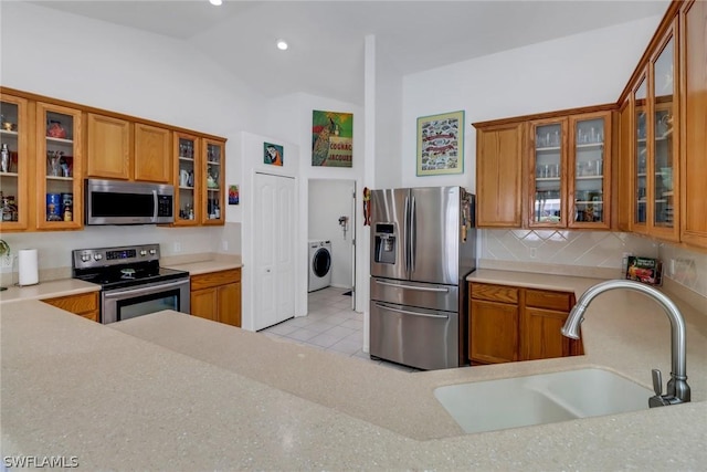 kitchen with sink, tasteful backsplash, washer / clothes dryer, vaulted ceiling, and appliances with stainless steel finishes