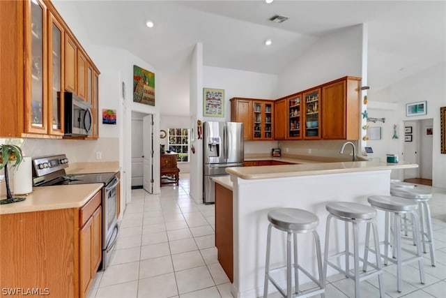 kitchen featuring kitchen peninsula, vaulted ceiling, a breakfast bar, light tile patterned floors, and appliances with stainless steel finishes