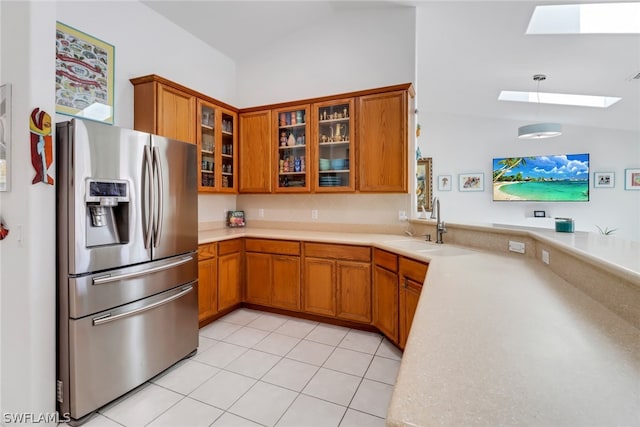 kitchen with sink, stainless steel refrigerator with ice dispenser, vaulted ceiling with skylight, decorative light fixtures, and light tile patterned flooring