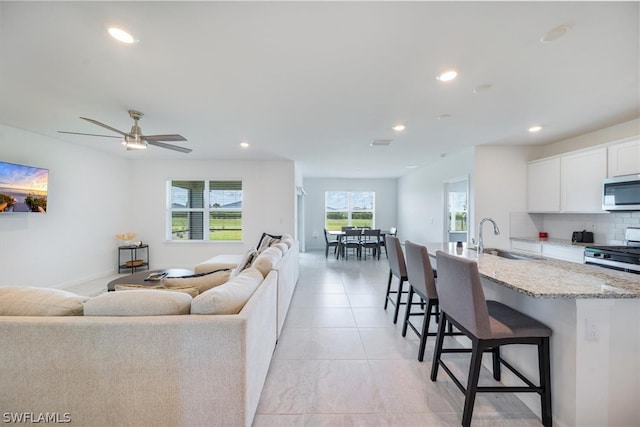 living room with ceiling fan, sink, and light tile flooring