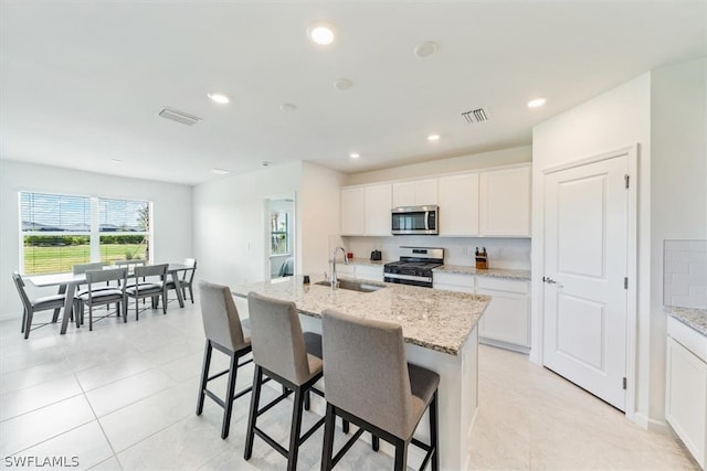 kitchen featuring appliances with stainless steel finishes, light tile floors, white cabinets, sink, and a center island with sink