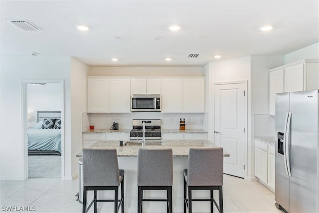 kitchen featuring stainless steel appliances, white cabinets, a center island with sink, and light tile flooring