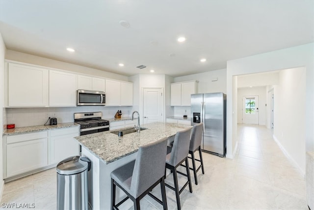 kitchen with stainless steel appliances, light tile floors, sink, and an island with sink