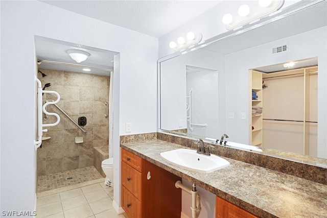 bathroom featuring tile flooring, tiled shower, vanity, and toilet