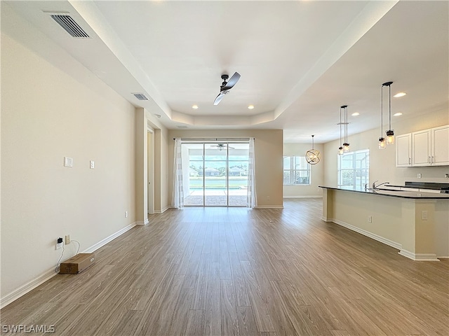 unfurnished living room with ceiling fan, a tray ceiling, and hardwood / wood-style flooring