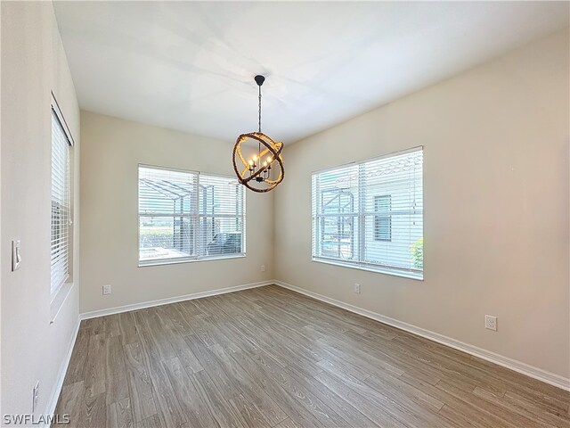 empty room featuring wood-type flooring and an inviting chandelier