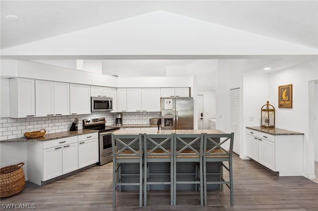 kitchen featuring a kitchen bar, backsplash, lofted ceiling, stainless steel appliances, and a kitchen island with sink