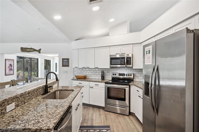 kitchen with stone counters, appliances with stainless steel finishes, light hardwood / wood-style flooring, lofted ceiling, and sink