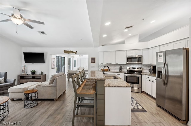 kitchen with white cabinets, appliances with stainless steel finishes, a kitchen bar, light stone counters, and tasteful backsplash