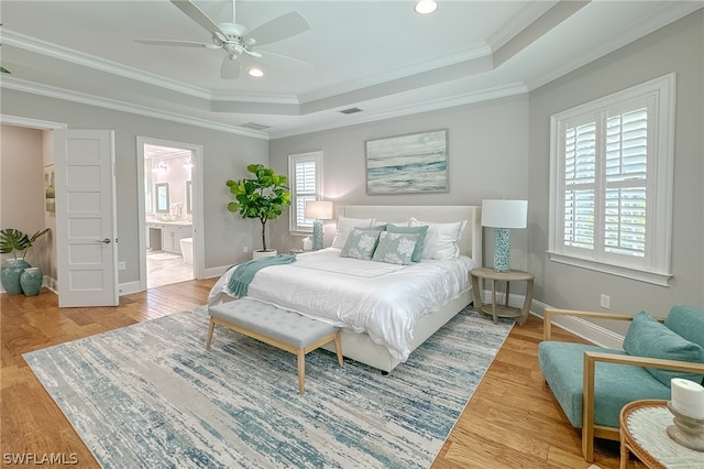 bedroom with ornamental molding, wood-type flooring, connected bathroom, and a raised ceiling