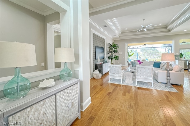 living room with crown molding, light hardwood / wood-style floors, ceiling fan, and a tray ceiling