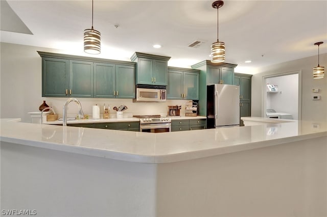 kitchen with washer / dryer, decorative light fixtures, kitchen peninsula, stainless steel appliances, and green cabinetry