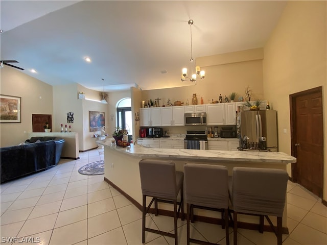 kitchen with hanging light fixtures, vaulted ceiling, stainless steel appliances, ceiling fan with notable chandelier, and white cabinetry