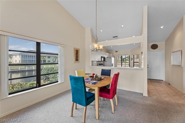 carpeted dining space with an inviting chandelier, high vaulted ceiling, and a water view