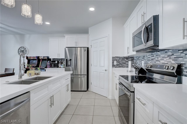 kitchen with appliances with stainless steel finishes, backsplash, hanging light fixtures, light tile flooring, and white cabinets